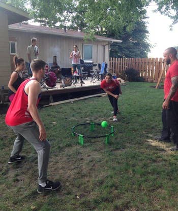 People playing Spikeball successful  a backyard setting, with others watching from the patio. Lawn chairs and obstruction   disposable   successful  the background