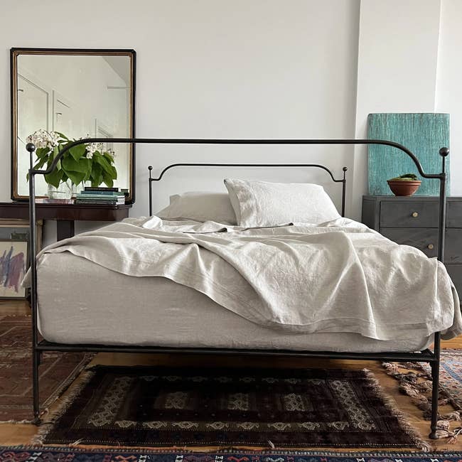 A tidy bed with plain bedding, set in a room with a vintage rug and minimalistic decor