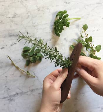 hands feeding a sprig of rosemary through the wooden herb stripper