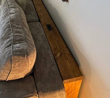 A wooden table wedged between the wall and a couch with outlets on it