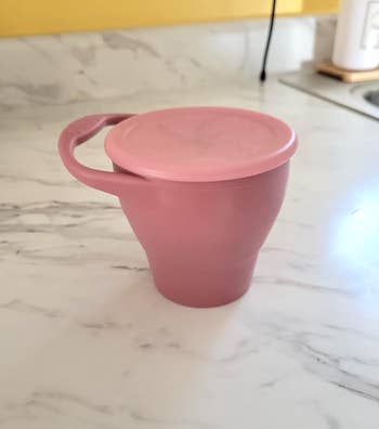 A reviewer's collapsible silicone cup with lid on a kitchen counter