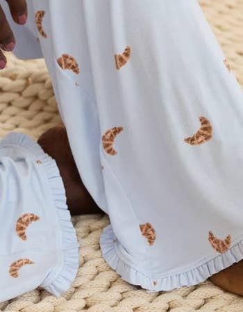 Person wearing pajama pants patterned with croissants, sitting connected  a woven rug