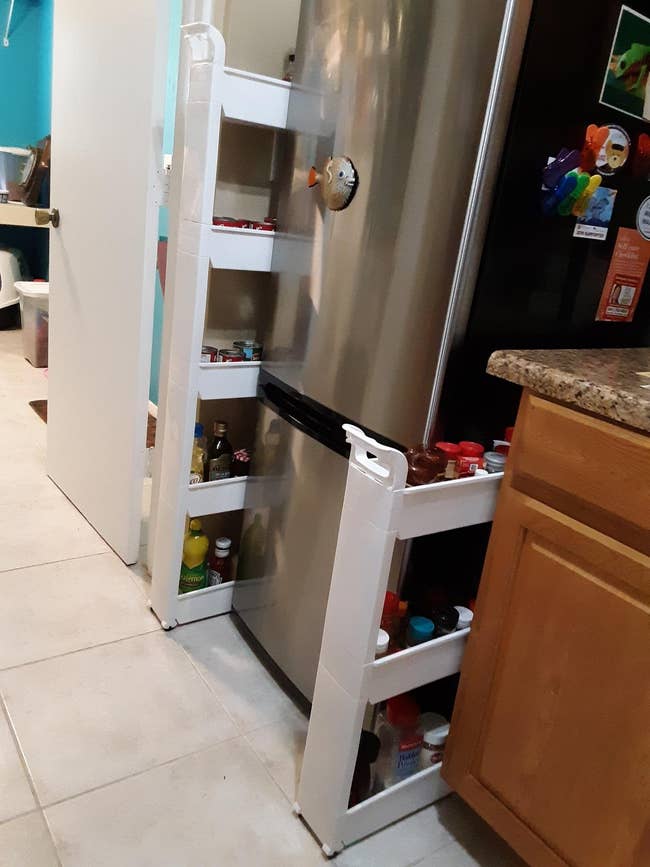 A kitchen showing the five-tier cart on the left side of the fridge filled with pantry ingredients and the three-tier cart on the right side with spices