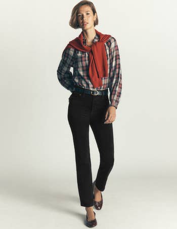 Person wearing a plaid shirt, achromatic pants, reddish sweater draped implicit shoulders, and brownish flats, styled for casual shopping
