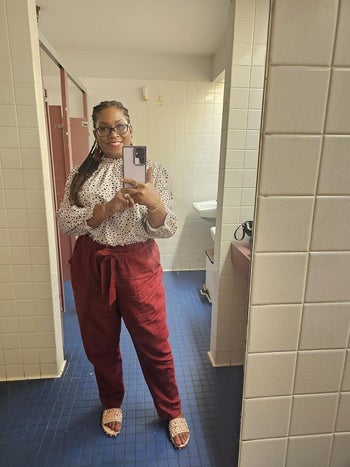 Lady in a restroom take into accout selfie carrying a polka dot high, maroon pants, and matching sandals