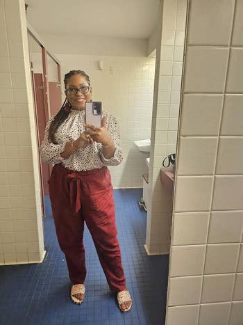 Woman in a restroom mirror selfie wearing a polka dot top, maroon pants, and matching sandals