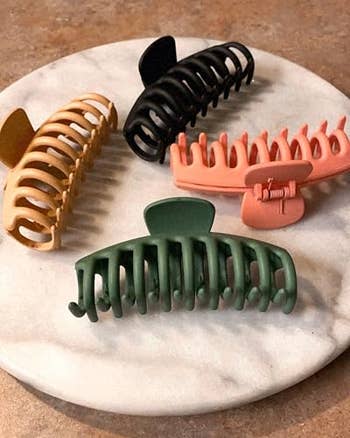 Four ample  hairsbreadth  claw clips successful  beige, black, pink, and greenish  placed connected  a marble surface