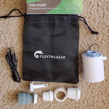 a reviewer photo of a small drawstring bag, the pump, and included attachment heads 