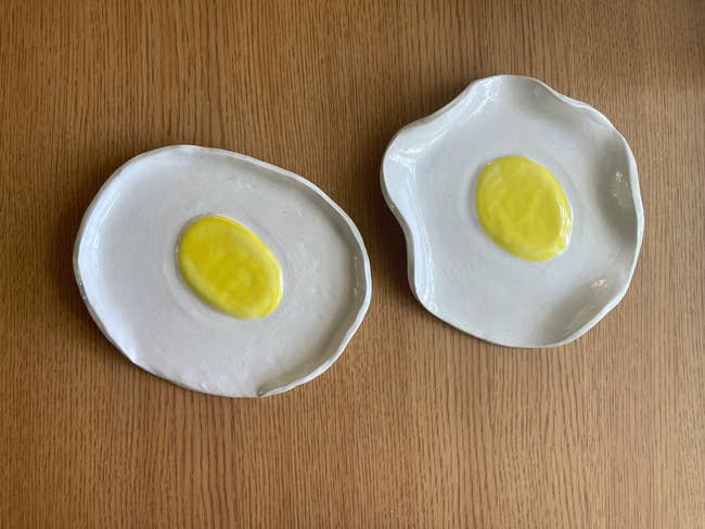 Two ceramic dishes shaped like fried eggs on a wooden surface