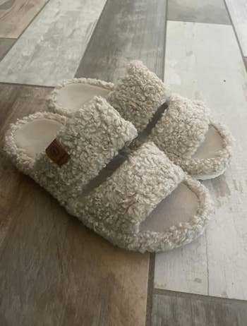 Fuzzy slippers with heavy straps connected a textured floor, perfect for cozy indoor comfort