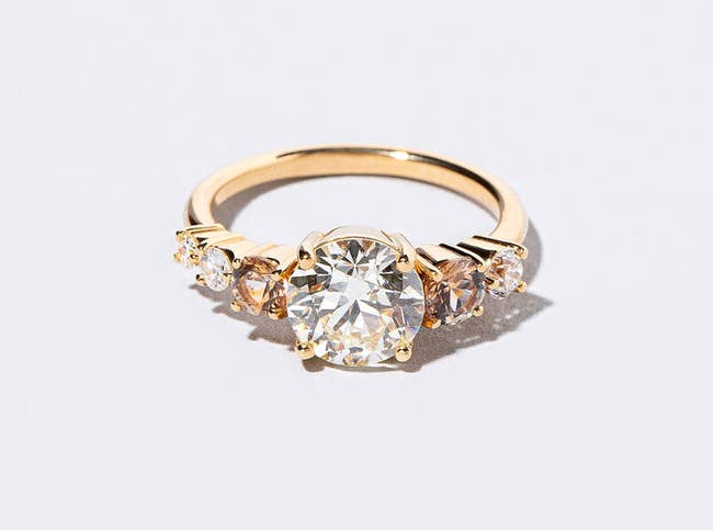 Gold ring with a central diamond flanked by smaller gems on a white background