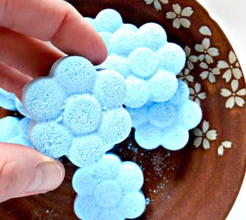 hands holding turquoise flower shaped toilet bombs