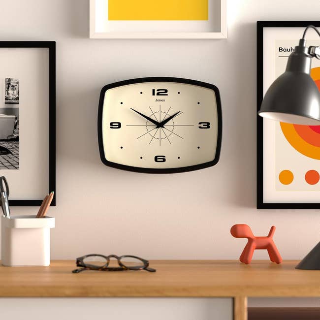 Wall-mounted square clock with a retro design, above a desk with decor items