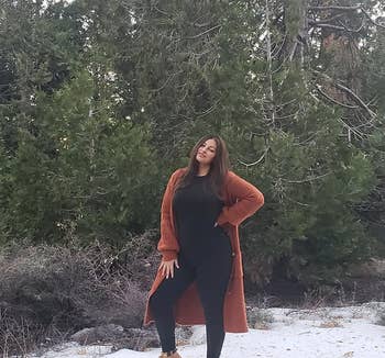 A reviewer in the black top and bottom set under a coat while outside in a snowy landscape