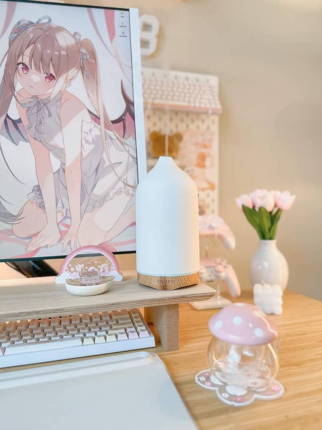 Computer table setup with anime quality illustration arsenic the show background, a achromatic aerial diffuser, pinkish gaming controller, and decorative items including a solid mushroom ornament
