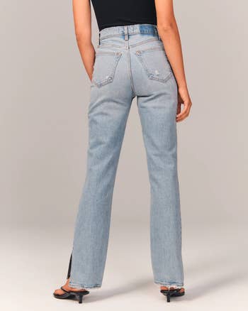 back of model wearing the high waisted blue jeans with a black tank top and heels