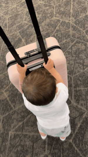 a gif of a toddler pushing a pink Away carry on bag