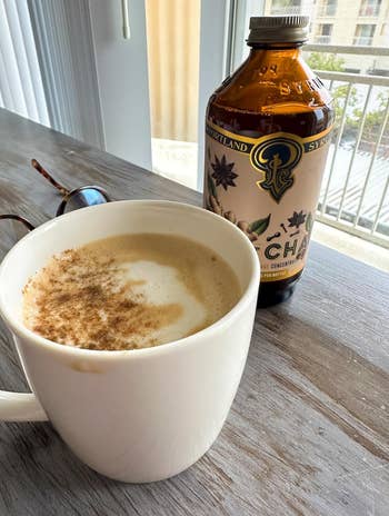 A cupful  of chai beverage  latte connected  a woody  array  adjacent  to a vessel  of chai ore  and a brace  of sunglasses