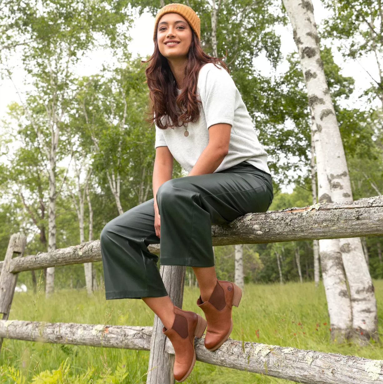 Model is wearing tan Chelsea boots while sitting on a wooden fence