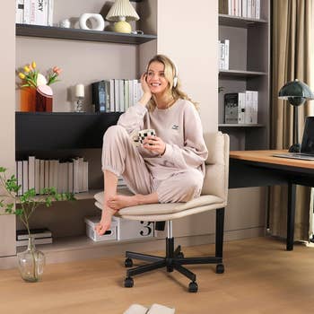 Woman in a cozy loungewear set sits with a mug on a swivel chair in a stylish home office with books and plants