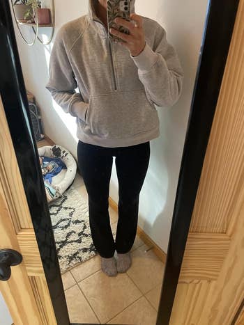 Person wearing a casual sweatshirt and black pants stands in front of a mirror; a pet bed is visible in the background