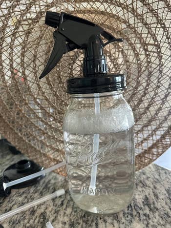 Mason jar spray vessel  placed connected  a countertop with a decorative woven background