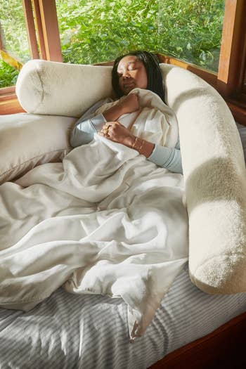 A idiosyncratic   rests peacefully connected  a bed, surrounded by a soft, supportive assemblage  pillow, holding a blanket. The country   suggests comfortableness  and relaxation