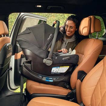 model securing a baby car seat in a vehicle's back seat