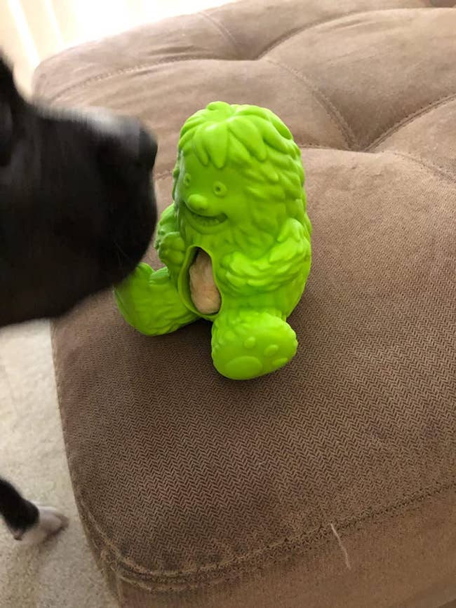 a green silicone toy shaped like a yeti with a square treat inside its belly