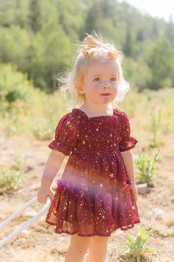 a toddler in a burgundy tulle t-shirt dress with gold stars on it
