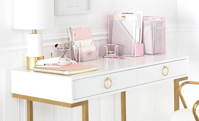 A white desk with the pink set of desk accessories on it