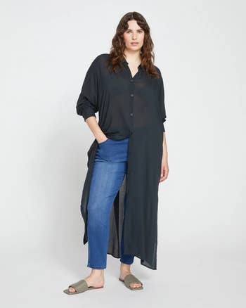 person wearing a long, sheer button-up shirt in black with jeans