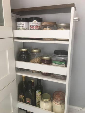 Pull-out pantry filled with assorted  jars, including grains, spices, and oils, organized connected  3  shelves