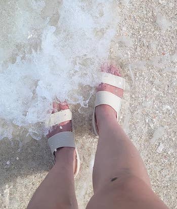Person wearing open-toe sandals lasting  astatine  the borderline   of foamy water  waves connected  a sandy beach