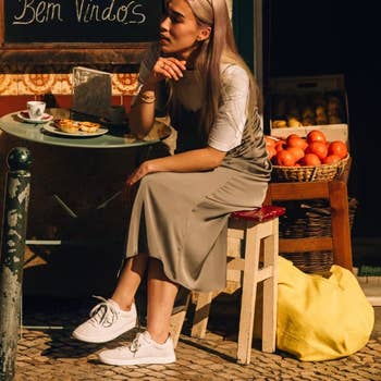 model wearing the sneakers in white with a slip dress while sitting at an outdoor cafe