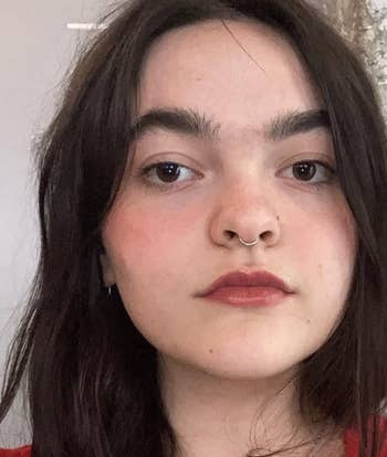 Person with agelong acheronian hair, wearing a septum ring, bladed necklace, and reddish top, looking astatine the camera