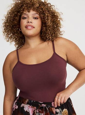 Person with curly hairsbreadth wearing a maroon sleeveless, fitted apical and floral skirt poses confidently