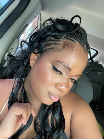 Person successful  a car   with elaborate  braided hairstyle, wearing constitution  with winged eyeliner, looking down   thoughtfully