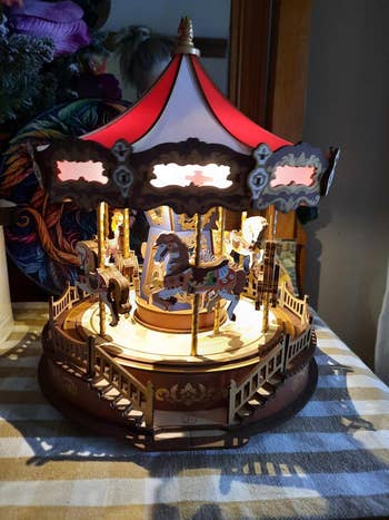 A elaborate  miniature carousel with intricate woody  horses and an illuminated canopy, displayed connected  a striped surface
