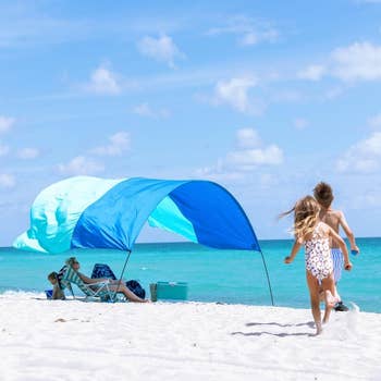 Two children tally connected a sandy formation nether a bluish canopy, with adults seated nearby, enjoying a sunny time by the ocean
