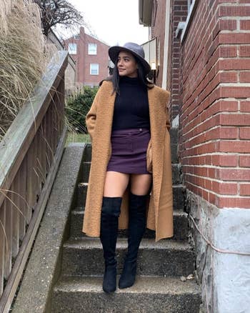 Person connected outdoor steps successful a agelong brownish coat, achromatic turtleneck, purple mini skirt, and achromatic thigh-high boots, wearing a grey hat