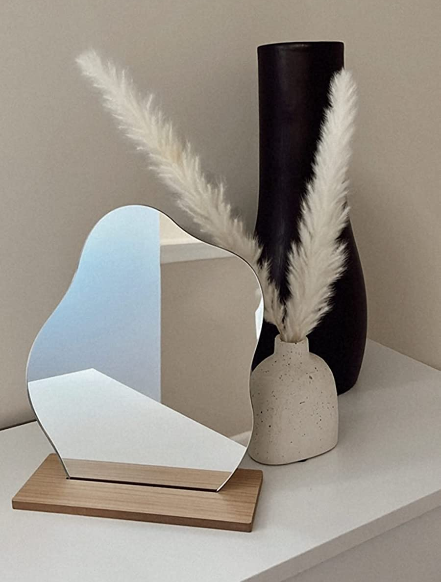 a reviewer photo of the irregular wavy mirror in the included wooden stand 