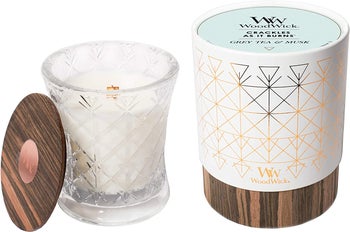 White candle with wooden wick in a clear glass jar next to product box