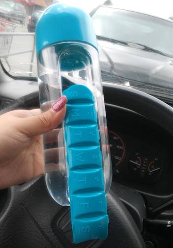 reviewer holding the blue and clear water bottle and showing how the pill organizer slides off