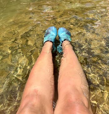 Person's legs successful h2o wearing bluish h2o shoes, with different radical lasting successful shallow h2o nearby