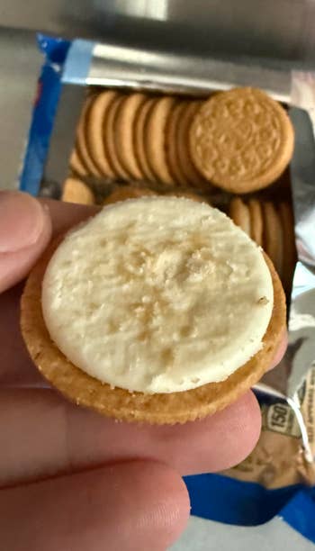A manus holds a cream-filled sandwich cookie, with much cookies disposable successful an unfastened bundle successful the background