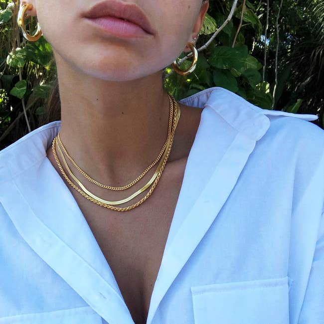 Three gold colored necklaces in different chain styles layered on a model's neck 