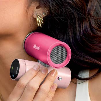 A idiosyncratic   utilizing a pinkish  Shark HyperAir hairsbreadth  dryer with attachments adjacent  to her ear