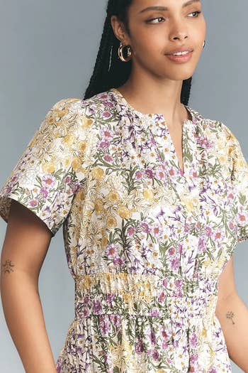 Model wearing a floral-patterned dress with short sleeves and a cinched waist, suitable for a summer or garden setting
