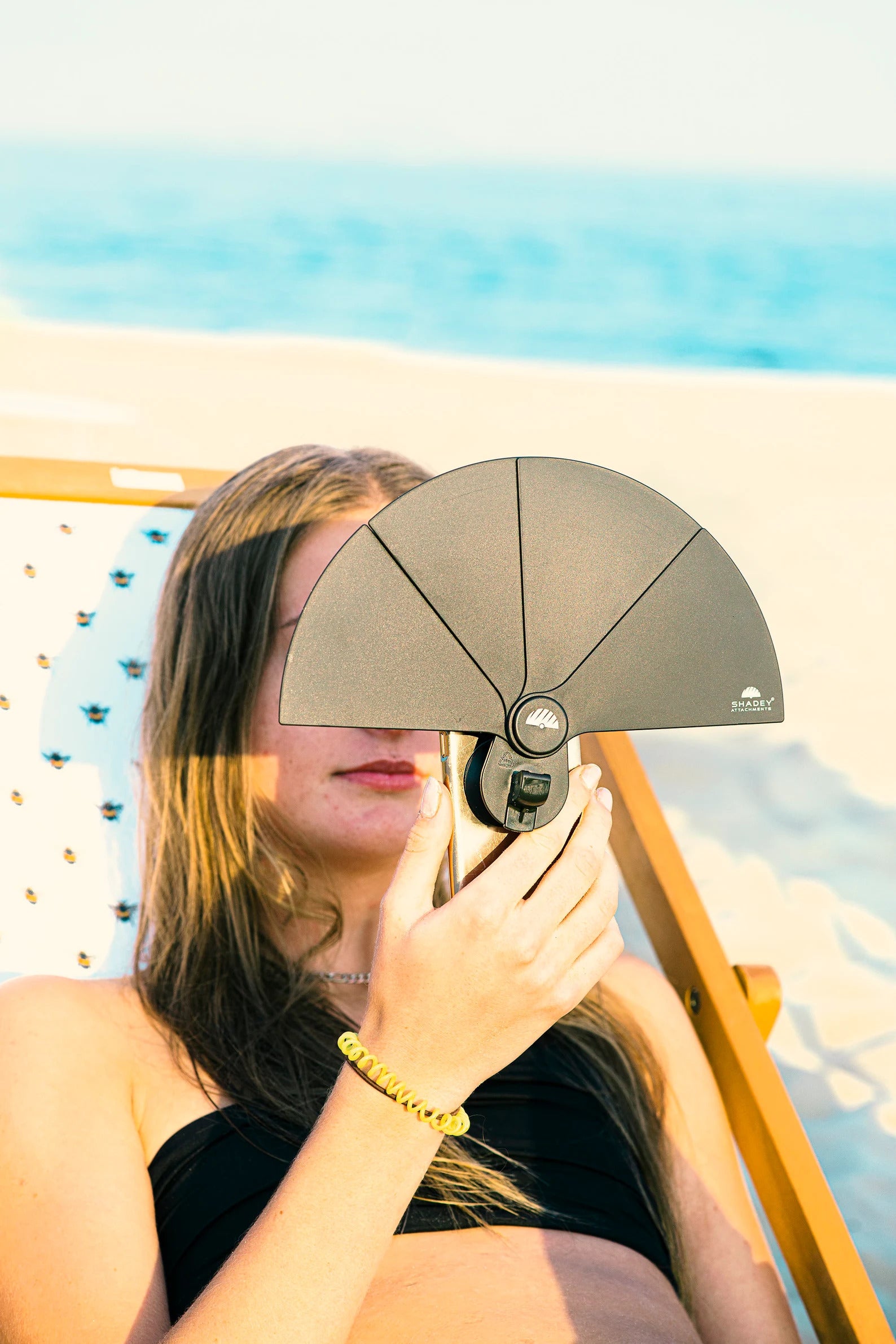 model holding up their phone, which has a black plastic fan-shaped attachment stuck to the back of it to block out sun